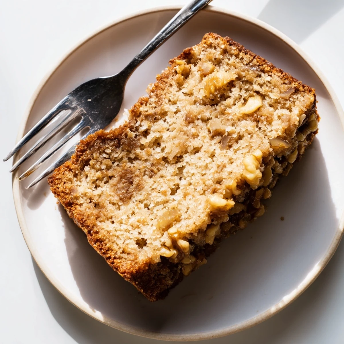 Sliced ultimate banana nut bread revealing moist texture and crunchy walnut pieces on a plate