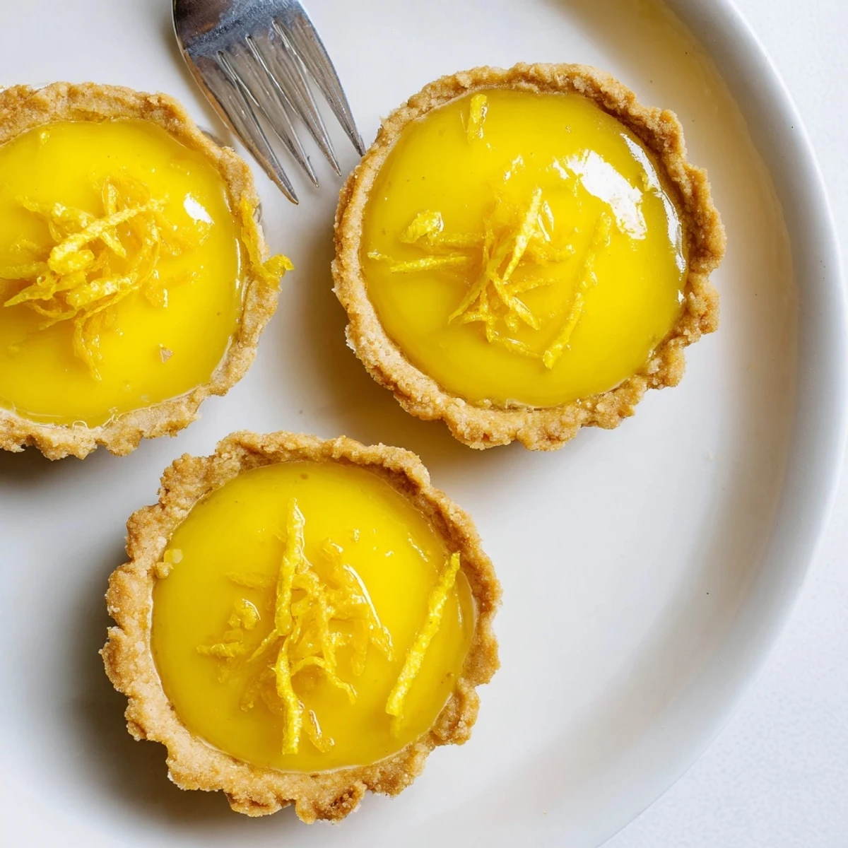 Bite-sized vegan lemon tarts featuring tangy coconut-based curd nestled in golden baked crusts perfect for spring desserts