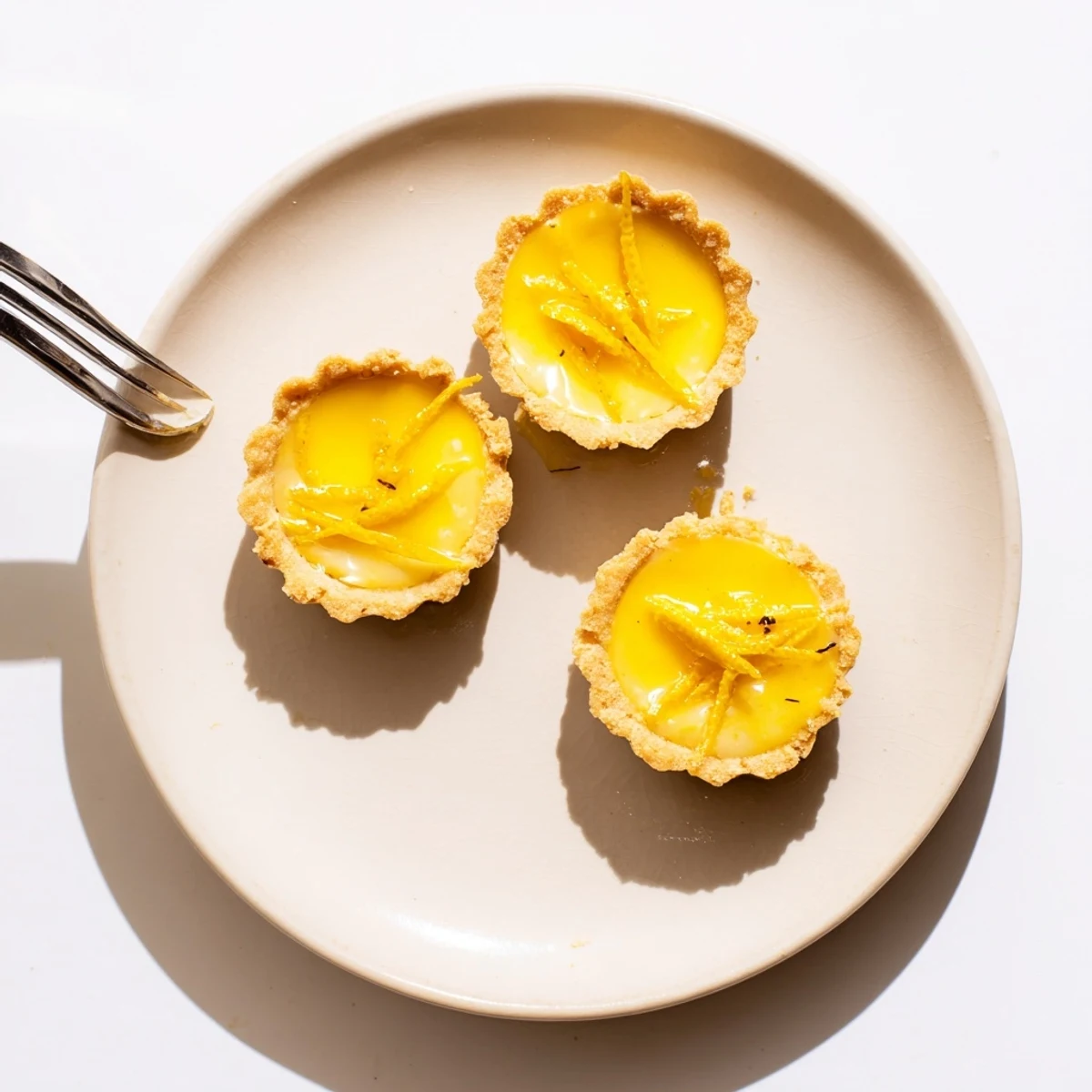 Vegan lemon tarts arranged on a white plate with bright citrus curd filling and optional fresh berry topping