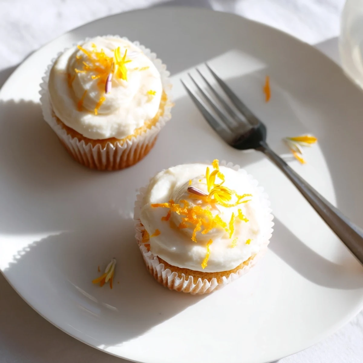 Golden-baked orange blossom cupcakes adorned with pastel frosting and edible flowers on a white serving plate