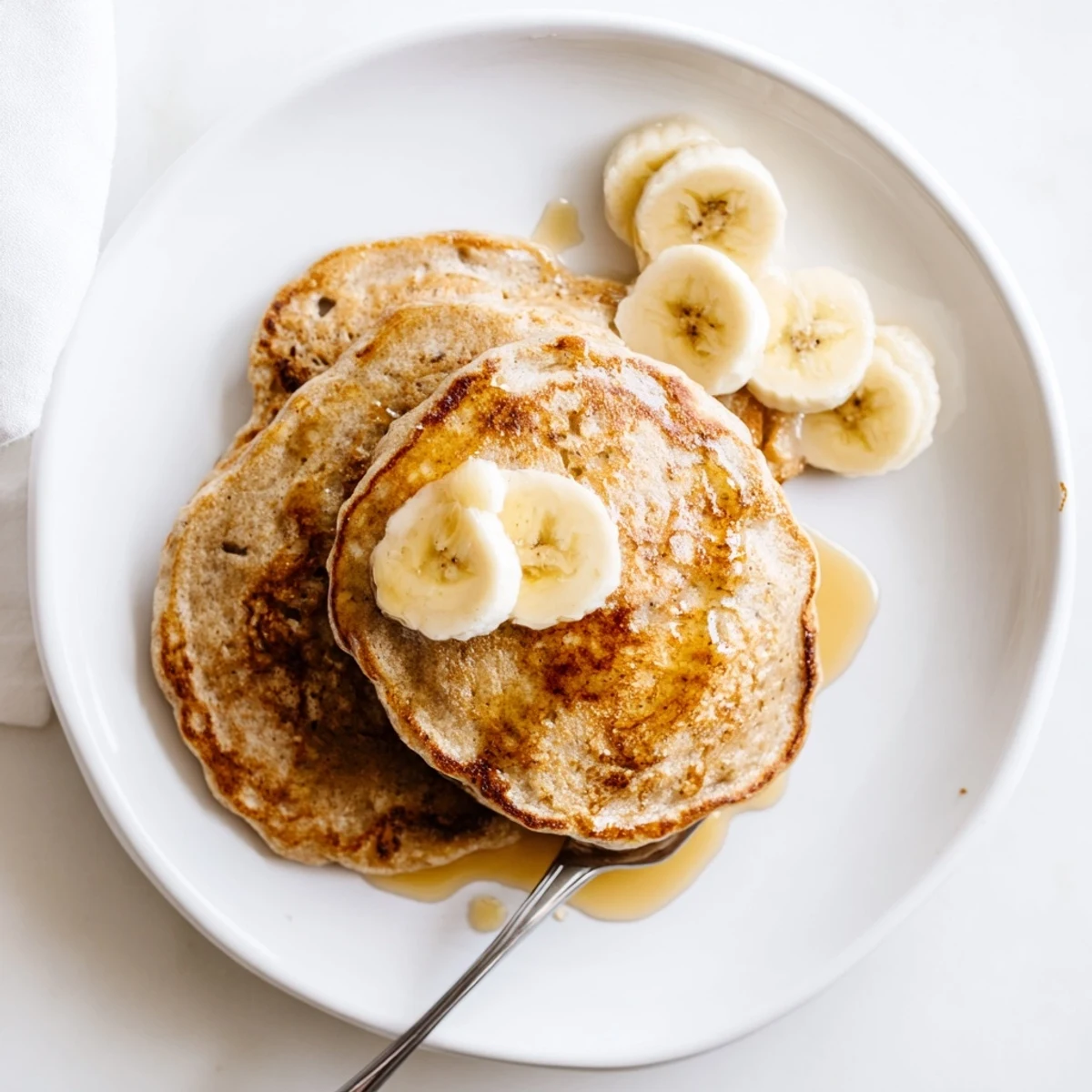 Protein-rich Greek yogurt banana pancakes stacked high with butter melting down the sides on a ceramic plate