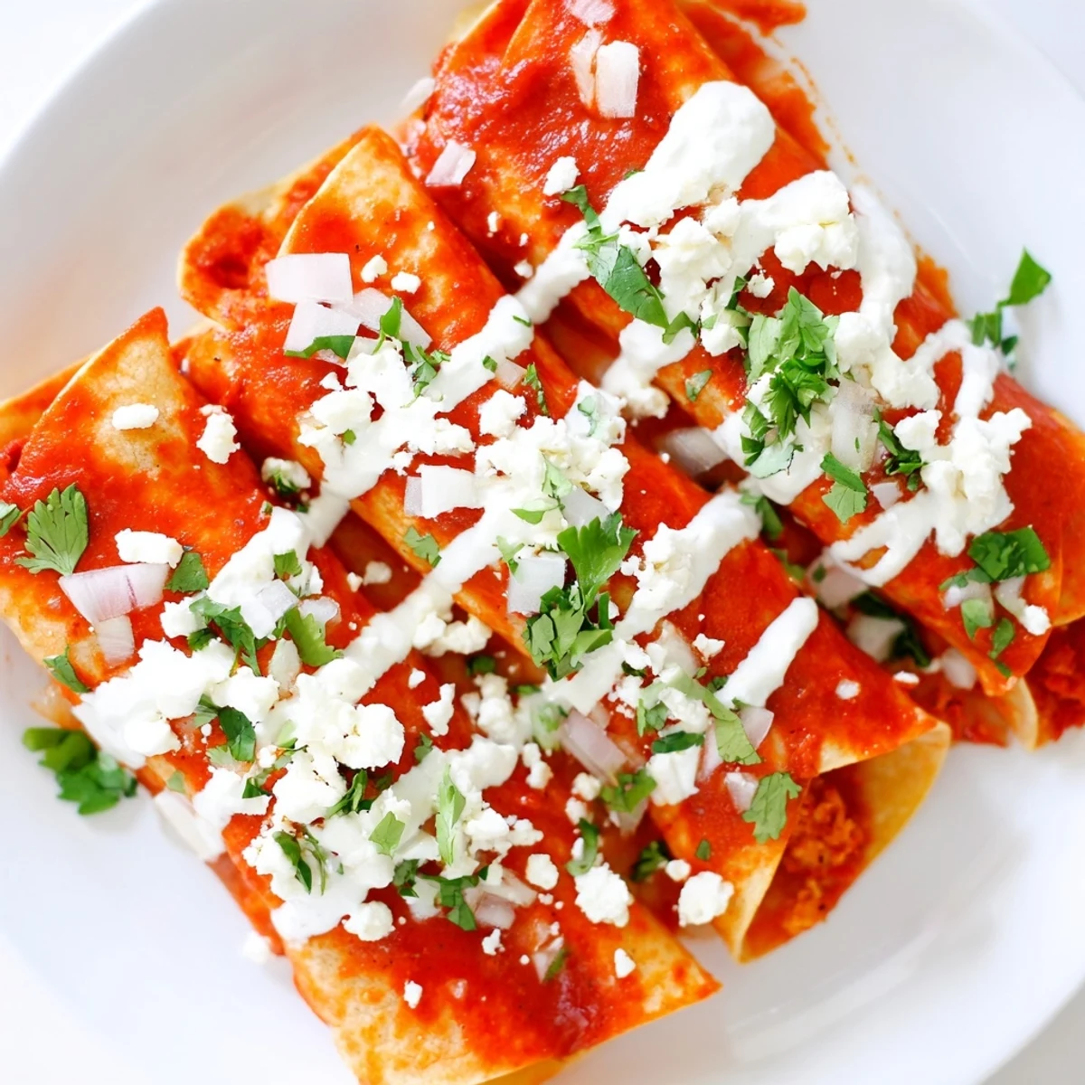 Warm corn tortillas coated in savory tomato sauce folded with creamy cheese and drizzled with Mexican crema