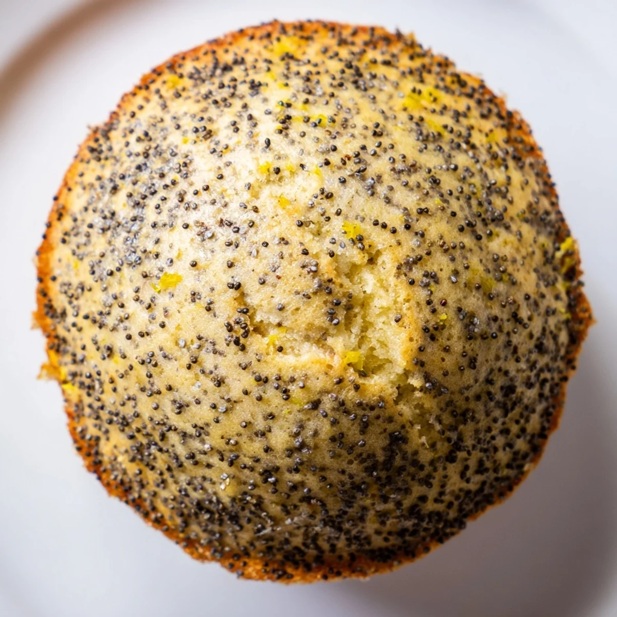 Moist lemon poppy seed muffins studded with tiny black seeds beside a bowl of fresh zest