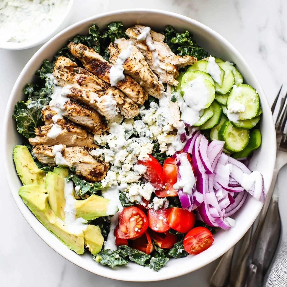 Juicy spiced chicken arranged over crisp bright kale alongside cherry tomatoes cucumber avocado and creamy feta crumbles