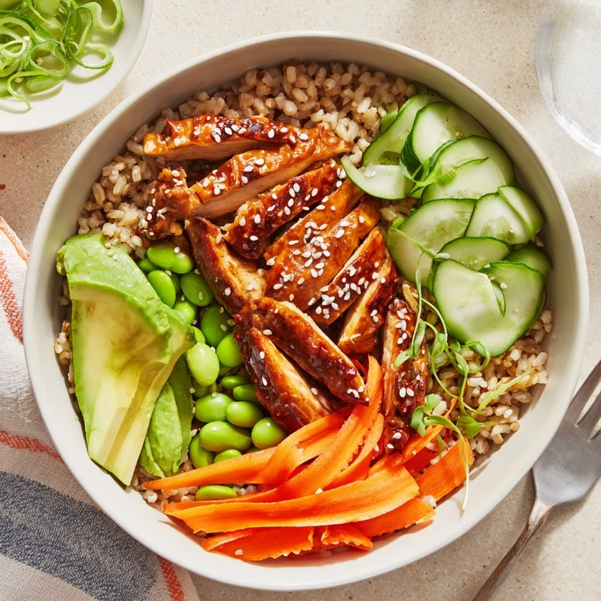 Glistening teriyaki chicken grain bowl topped with avocado and sesame seeds