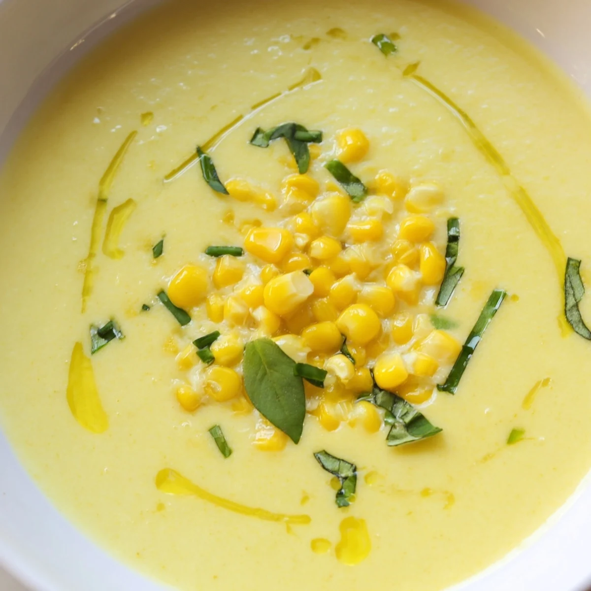 Creamy summer sweet corn gazpacho served chilled in a bowl with fresh basil garnish