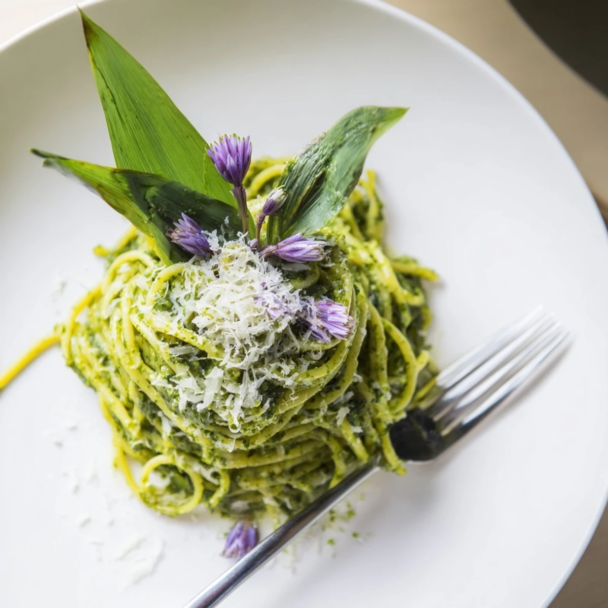 Steaming bowl of wild garlic pesto pasta topped with shaved Parmesan and fresh leaves.