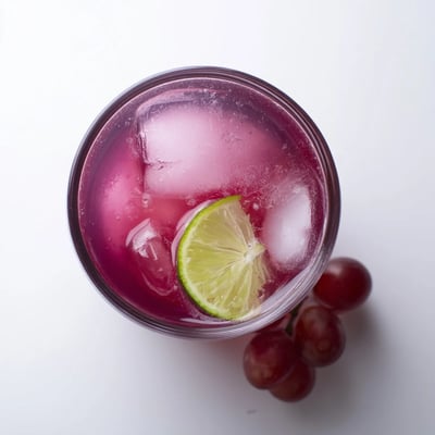 Vibrant purple grape agua fresca in a tall glass with lime wedges