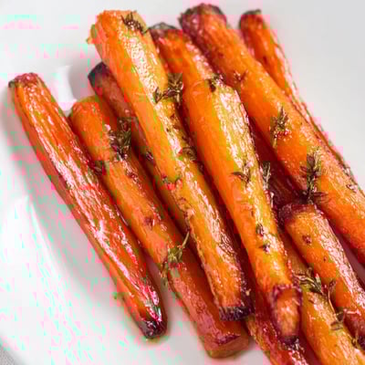 Crispy-edged honey roasted carrots scattered with fresh thyme in a white bowl