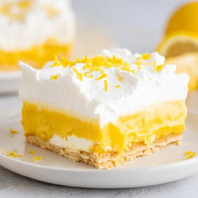 Creamy lemon lush cake dessert sliced into squares showing buttery crust and tangy pudding layers