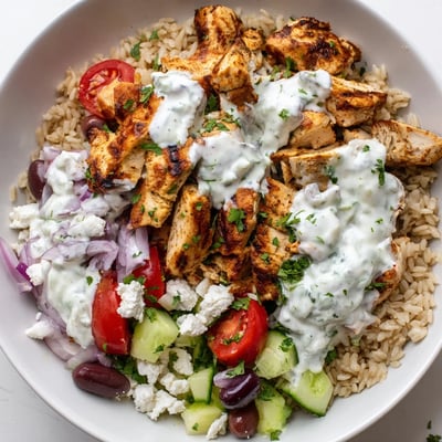 Vibrant Greek chicken grain bowl layered with cucumbers olives feta and creamy sauce.