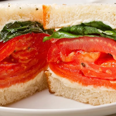 Golden sandwich bread piled high with thick tomato slices and fragrant basil leaves ready to bite